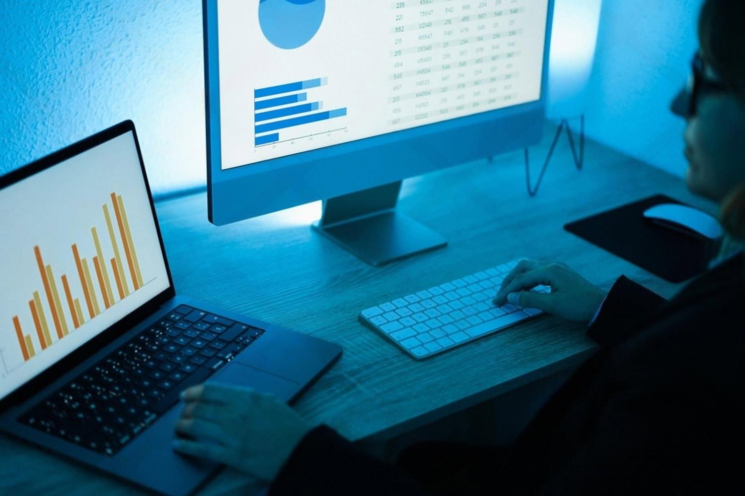 Analyst reviewing digital risk dashboards on a laptop and desktop monitor in a dim office