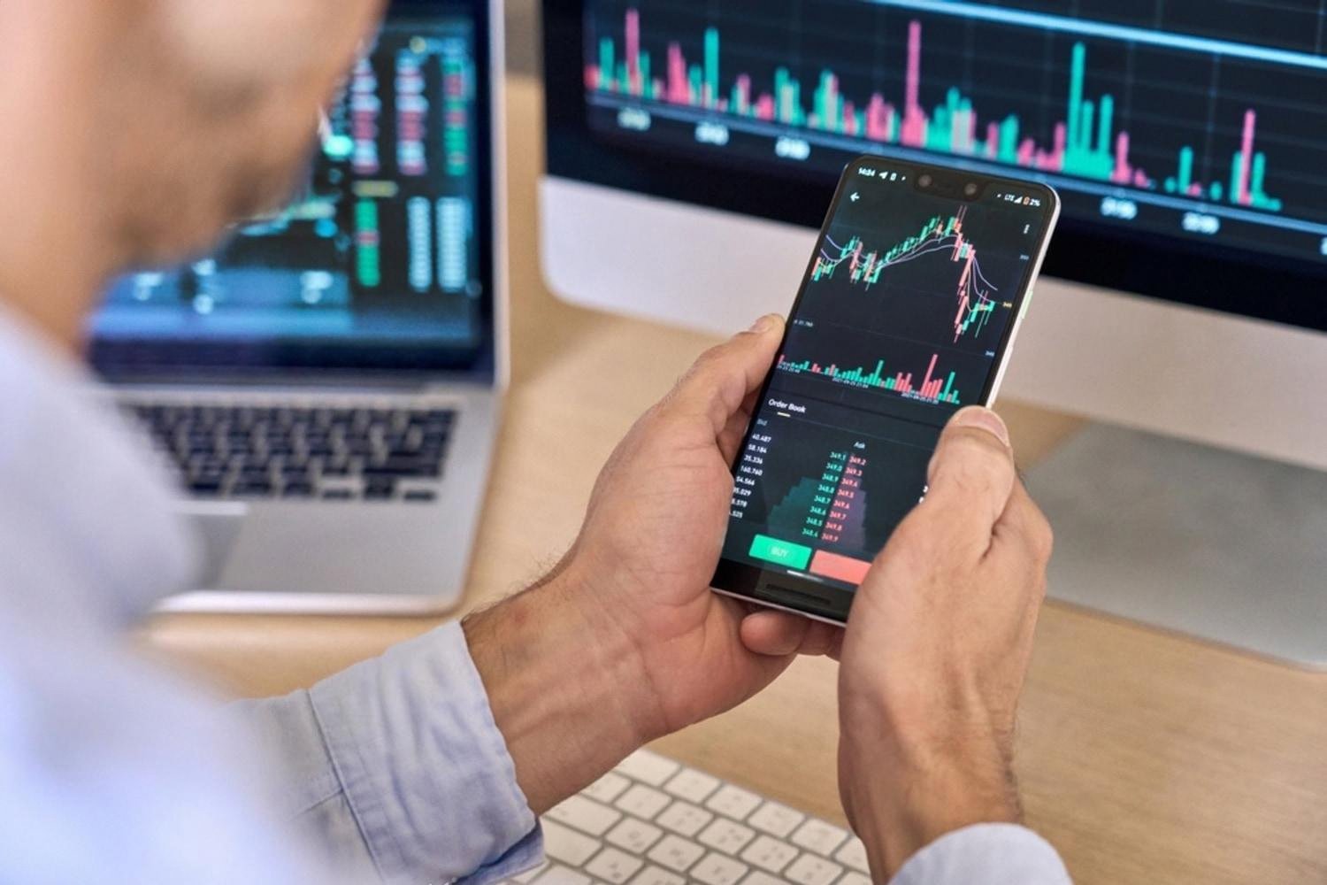 Manager checking real-time risk indicators on a smartphone next to trading-style monitors